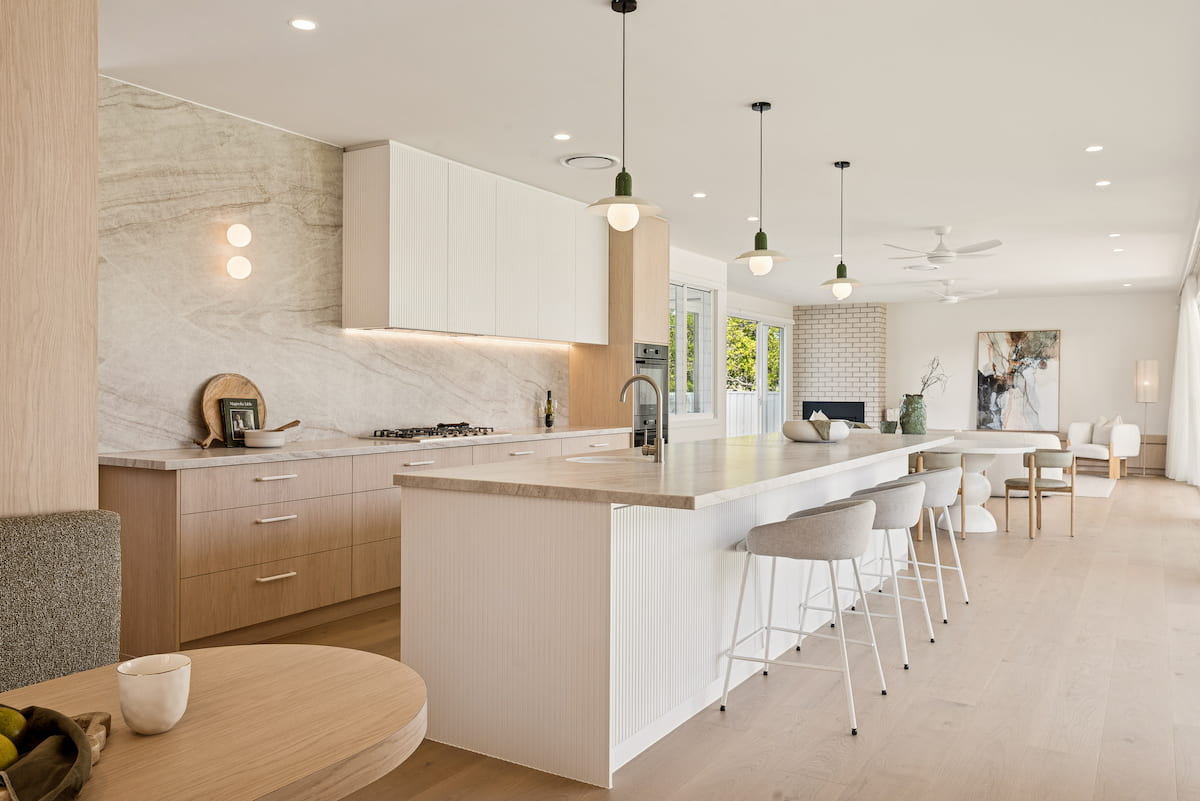Open plan kitchen with stone island bench, oak cabinetry and pendant lights